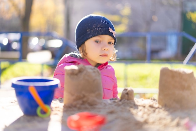 小さな子供が上着と帽子をかぶって砂場で遊んでいる