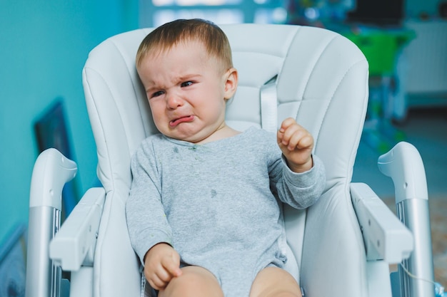 小さな子供がハイチェアに座って泣いている 授乳用のベビーチェア 小さな子供が座っている 子供の感情