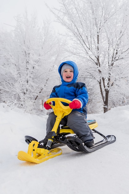Un bambino piccolo è seduto su uno scooter da neve in inverno