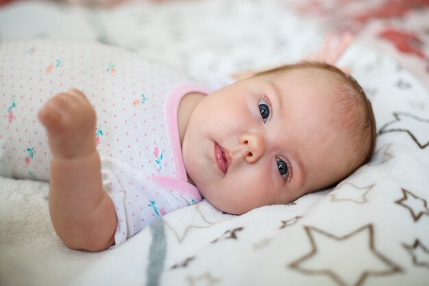 A small child lies on a white sheet. Baby clothes that lie in the crib