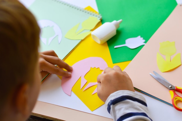 A small child makes paper crafts for mother's day or birthday A boy makes paper flowers for mom A simple pleasant idea of a children's gift to mom