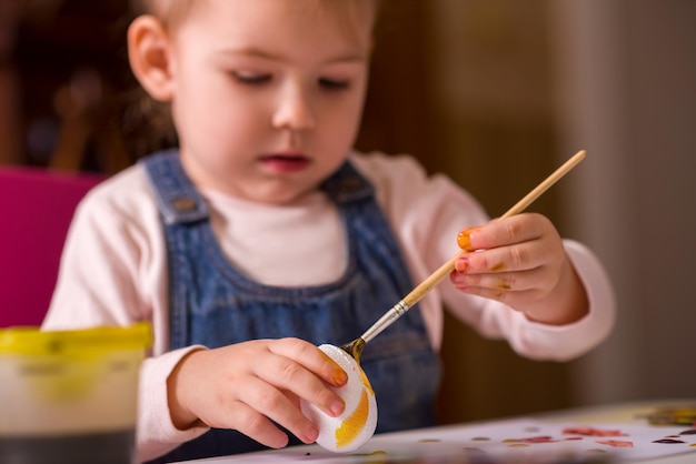 A small child paints eggs with colored paints for Easter