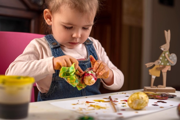 A small child paints eggs with colored paints for Easter