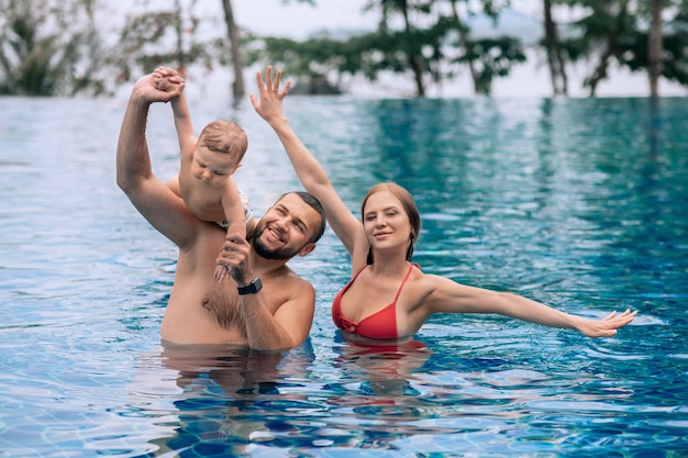 A small child and parents having fun in swimming pool on summer holiday 