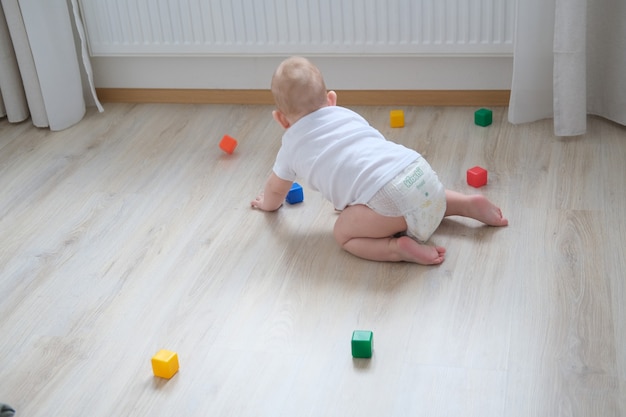Маленький ребенок играет на полу с разноцветными кубиками и строит из них пирамиду.