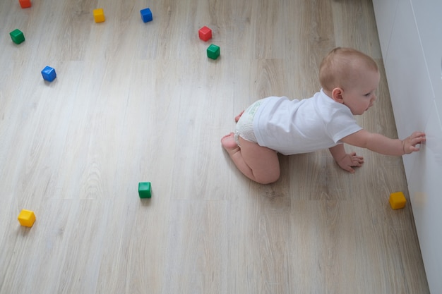 A small child plays on the floor with colored cubes and builds a pyramid out of them.