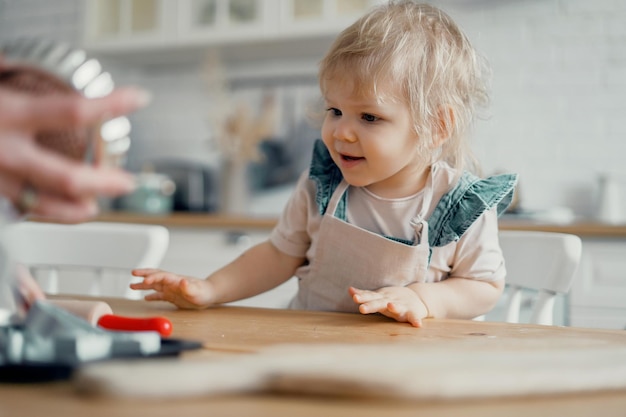 Un bambino piccolo gioca con sua madre sul tavolo con gli ingredienti farina e zucchero per una torta