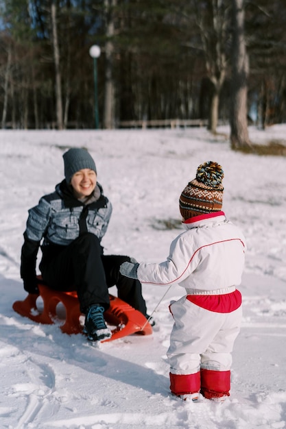 小さな子供が雪の平原の裏側の景色でスレードで笑う母親に乗っています