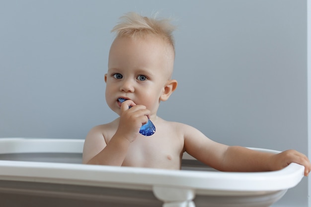 A small child rushes his teeth while sitting in the bathroom