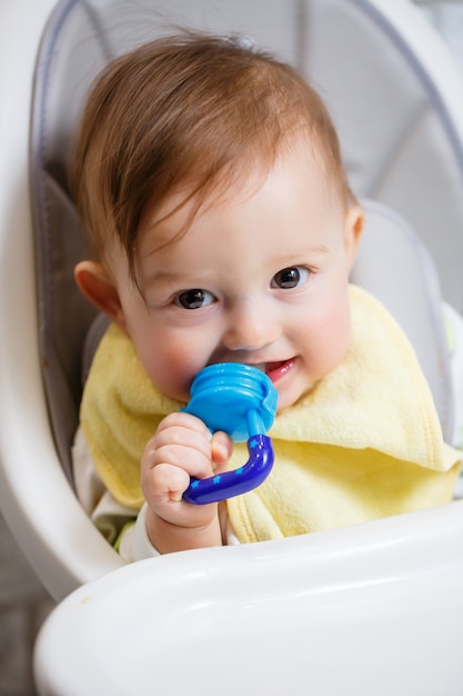 Un bambino piccolo si siede su un seggiolone e mangia la frutta attraverso la rete. nibbler per l'alimentazione dei bambini