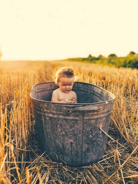 A small child sits in a large iron bathing basin in a field of mown wheat