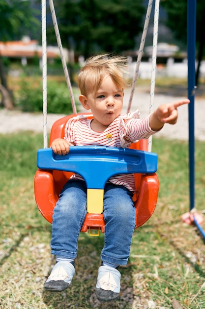 Small child sits on a swing and points somewhere with a finger