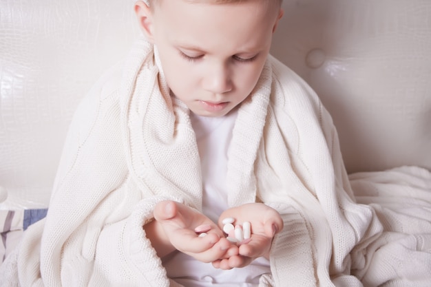 A small child sitting in a bed and holding in his palm pills