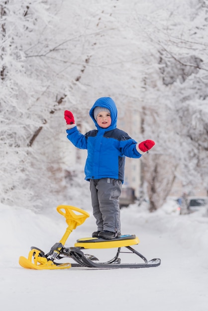 A small child stands on a snow scooter in winter