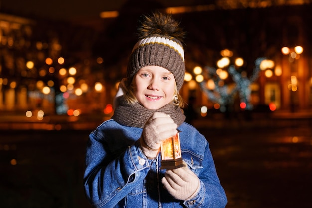 Small child waits for santa claus on street of small town during snowfall on christmas eve boy is ho...