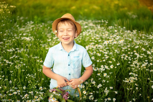 A small child walks through a field of daisies holds a basket of flowers in his hands smiles