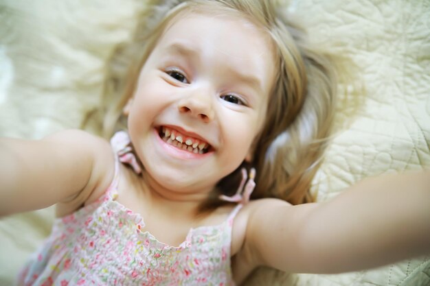 A small child with blond hair lies on the bed Baby girl is playing on the couch