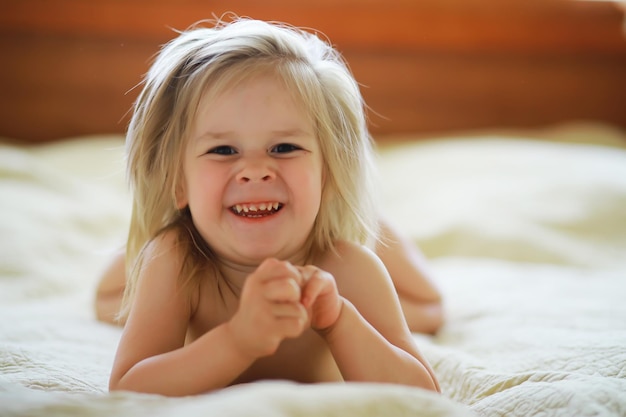 A small child with blond hair lies on the bed Baby girl is playing on the couch