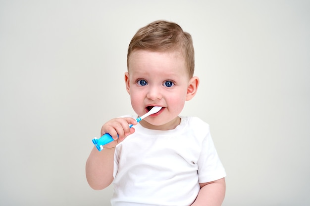 Un bambino piccolo con gli occhi azzurri tiene in mano gli spazzolini da denti.