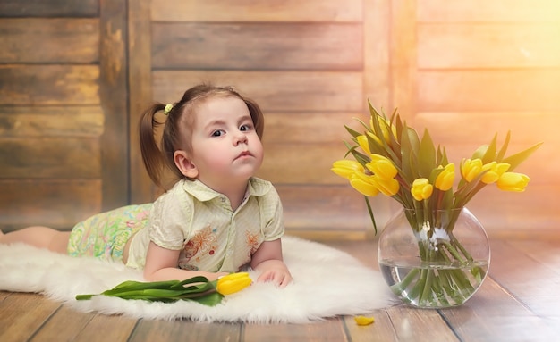 黄色いチューリップの花束を持つ小さな子供。花瓶に花の贈り物を持った少年。床に黄色いチューリップが付いている女性の休日の女の子への贈り物。