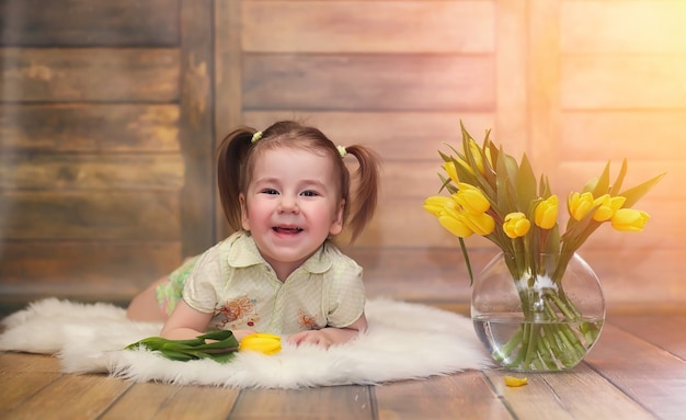 黄色いチューリップの花束を持つ小さな子供。花瓶に花の贈り物を持った少年。床に黄色いチューリップが付いている女性の休日の女の子への贈り物。