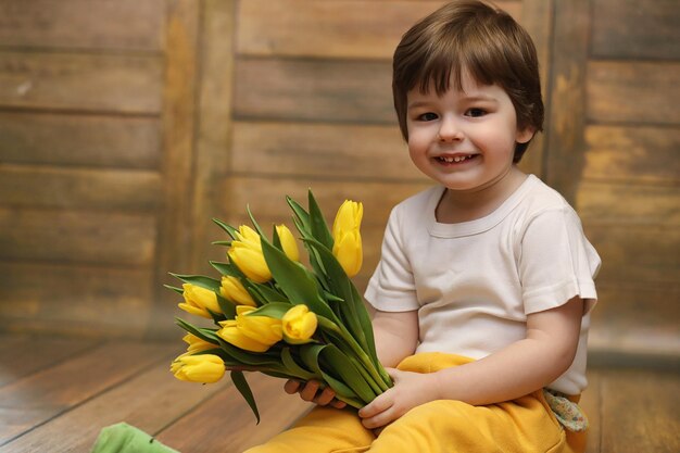 A small child with a bouquet of yellow tulips A boy with a gift of flowers in a vase A gift for girls on female holiday with yellow tulips on the floorxA