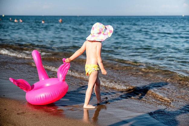 Small child with inflatable pink flamingo walking into the sea