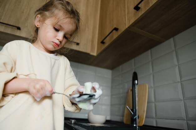 手にぼろきれを持った小さな子供が流しの近くの椅子に立って皿洗いをしている小さな女の子が母親の台所での料理と掃除を手伝っています