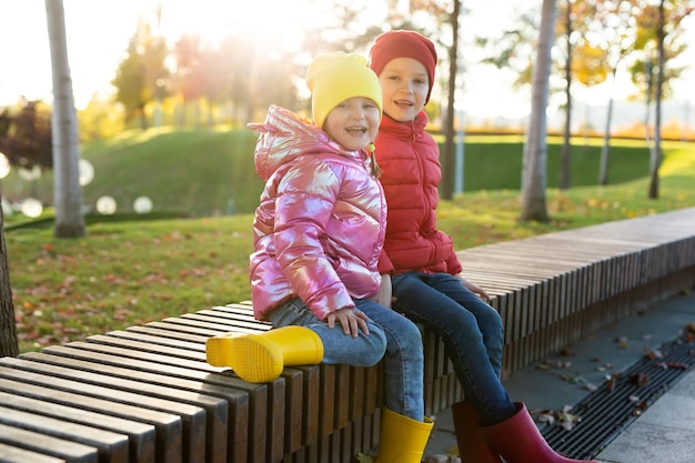 Small children brother and sister in rubber boots and bright clothes in the autumn park