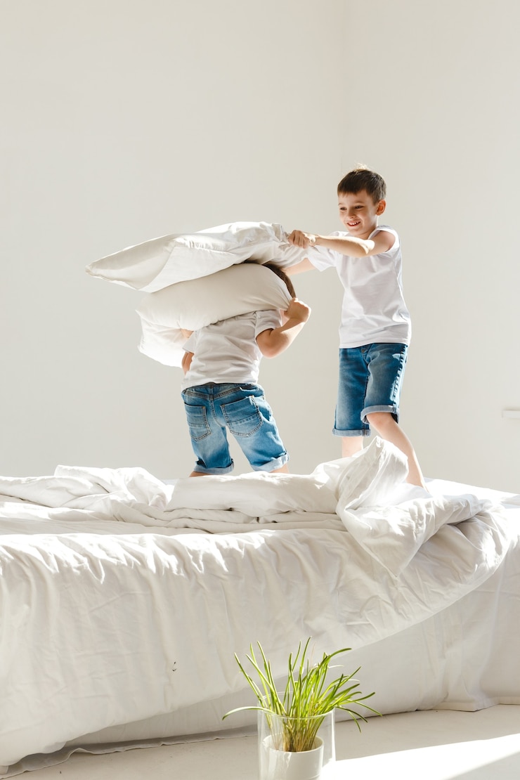 Photo small children jumping on a bed and having fun fighting with pillows in sunshine.
