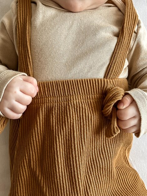 Small children's hands hold suspenders on brown pants a small child on a white background is close