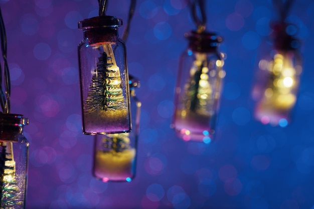 Маленькая новогодняя елка в стеклянной банке с гирляндой веселого Рождества фон неоновый боке