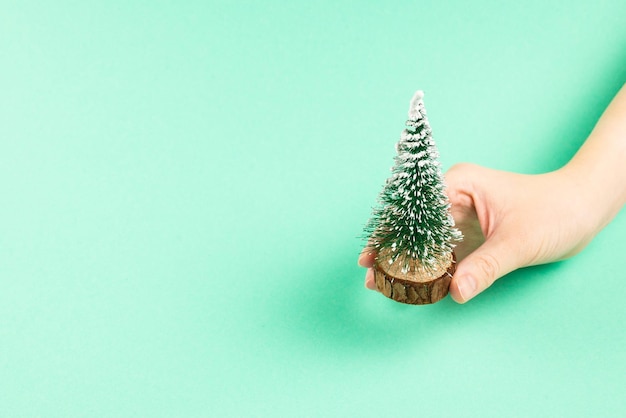 Small christmas tree in woman hand on a green background Copy space