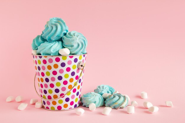 Small colorful bucket filled with blue meringue and white marshmallows on a pink pastel background
