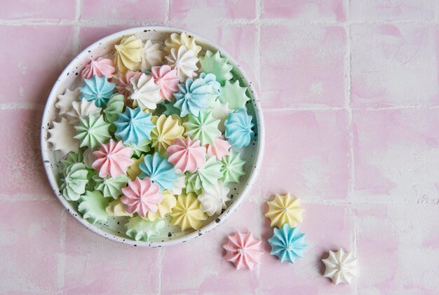 Photo small colorful meringues in the ceramic bowl on pink tile background