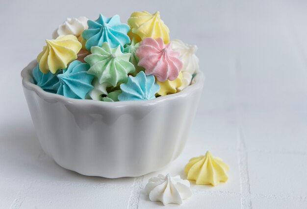 Small colorful meringues in the ceramic bowl on tile background