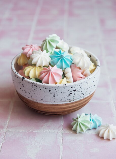 Small colorful meringues in the ceramic bowl on tile background