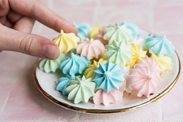 Photo small colorful meringues in the  ceramic plate on pink tile background