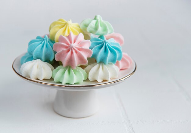 Small colorful meringues on the ceramic  stand on tile background