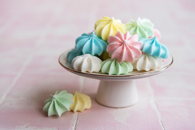 Small colorful meringues on the ceramic  stand on tile background