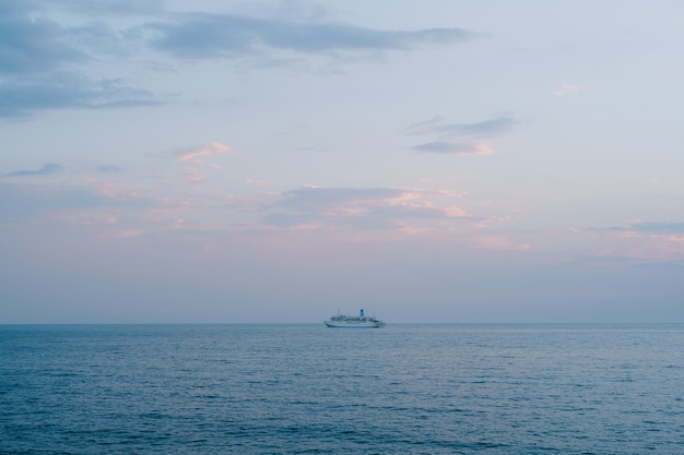 Una piccola nave da crociera naviga in mare aperto contro il cielo al tramonto con nuvole arancioni