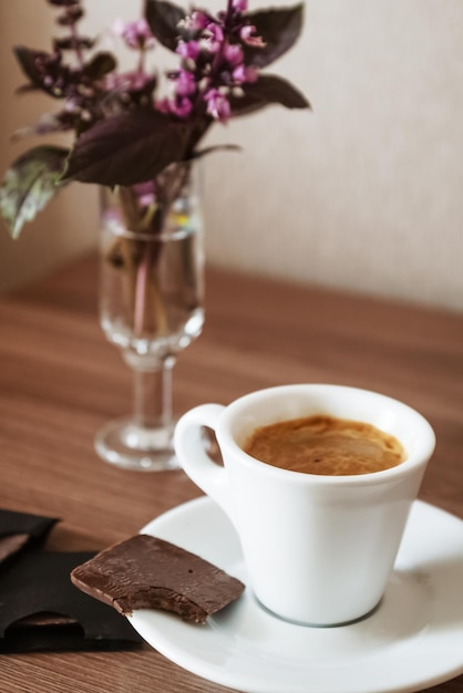 Small cup of espresso with bitten piece of chocolate on saucer at table surface