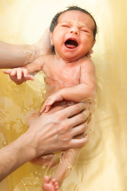 Small cute big-eyed beautiful baby bathes in warm water in the hands of a caring mother. The concept of baby care and child care