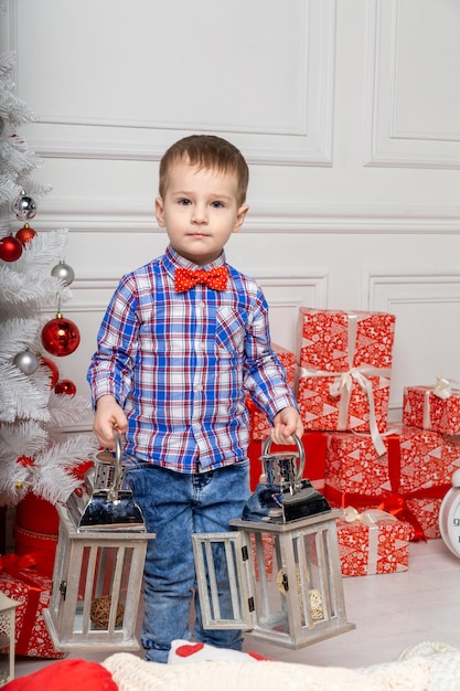 Small cute boy casual dressed standing in white room among christmas decorations