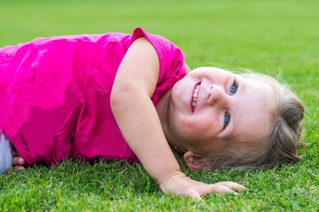 緑の芝生に横になってポーズをとる小さなかわいいヨーロッパの女の子。