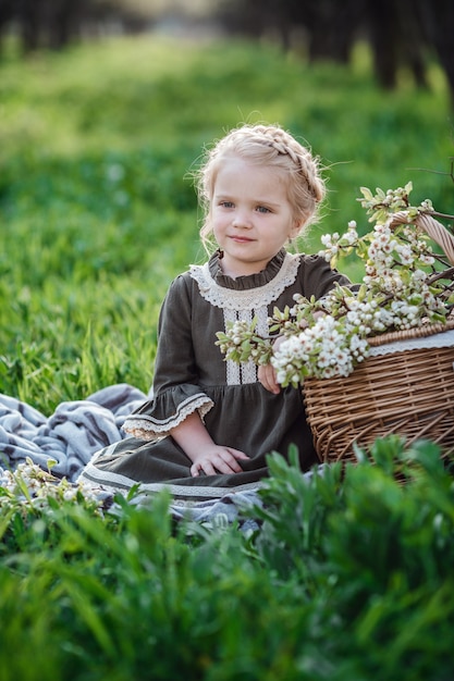 Small cute girl in dress in blossom garden. Cute baby girl 3-4 year old holding flowers over nature. Spring portrait. Aromatic blossom and retro vintage concept.