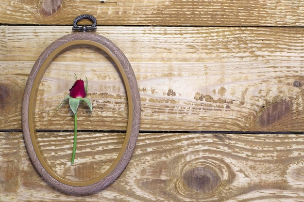 茶色の木の背景に木製の織り目加工のフレームで小さなかわいい赤いバラのつぼみをクローズ アップ