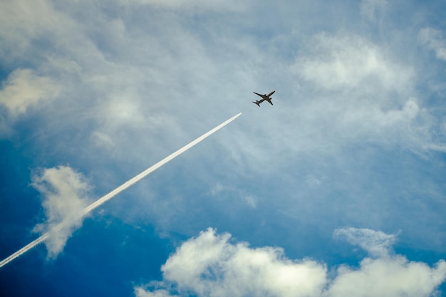 Small dark airplane silhouette flying high up in the blue cloudy sky The aircraft in the sky Airplane condensation trace Traveling by plane
