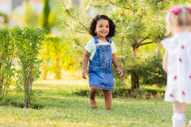 A small darkskinned girl with curly hair in a denim sundress walks on the street on a sunny day