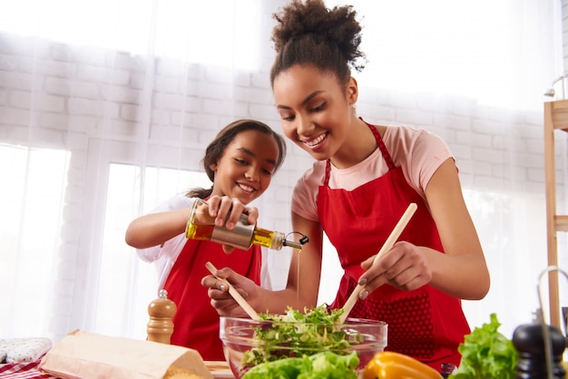 Small daughter pours olive oil into salad